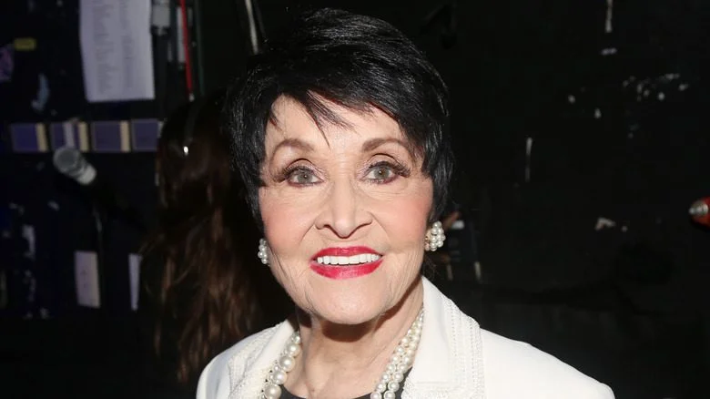 Chita Rivera souriante avec des boucles d'oreilles de perles et un collier lors d'un événement