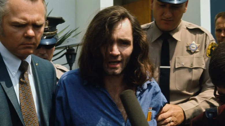Charles Manson avec la police parlant dans un microphone