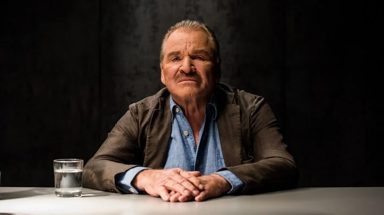 Fritz Wepper assis à une table, veste marron.