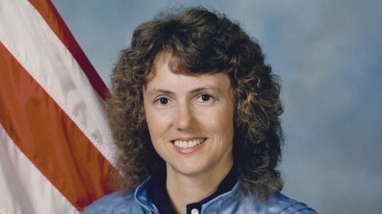 Christa McAuliffe souriante devant un drapeau