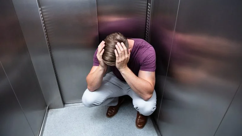 Homme accroupi piégé dans un ascenseur