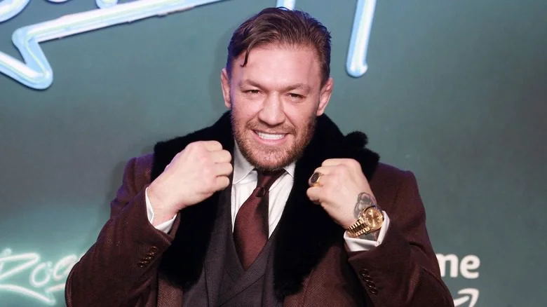 Conor McGregor en costume marron, souriant avec les poings levés