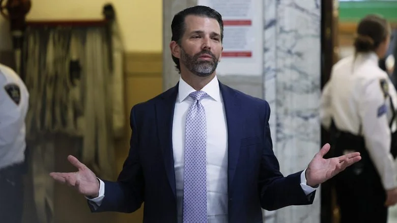 Donald Trump Jr. en costume bleu avec la barbe et les mains levées