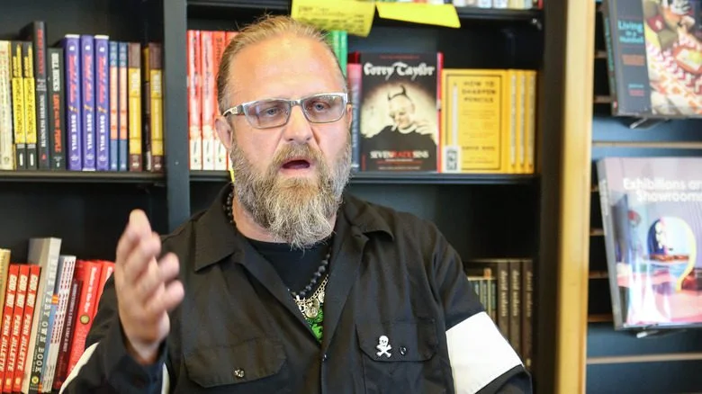 Shawn Crahan parlant, bras levé, dans une bibliothèque