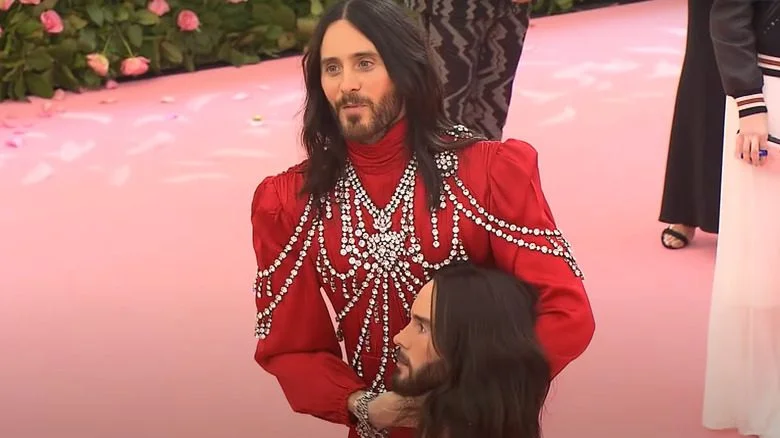 Photo de Jared Leto en robe rouge, diamants, tenant une réplique de sa tête