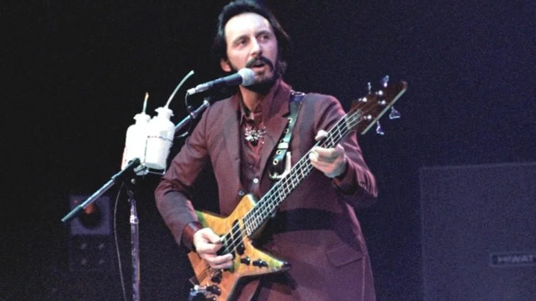 John Entwistle jouant de la basse sur scène avec un costume bordeaux