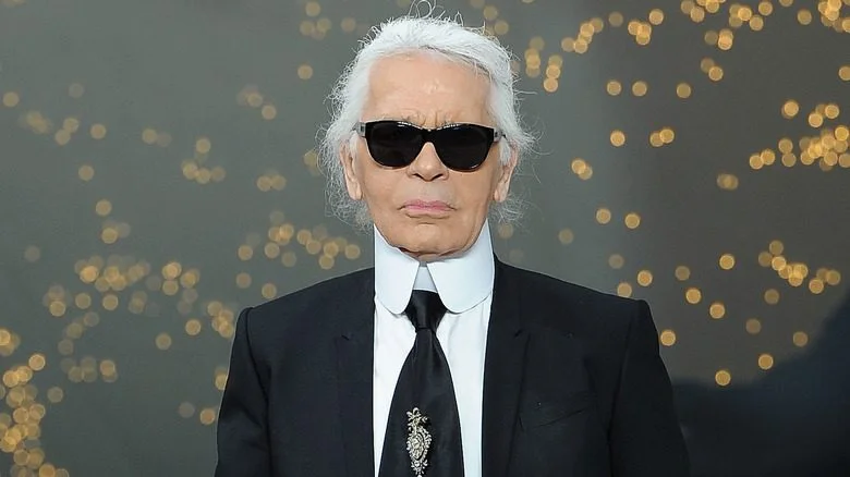 Karl Lagerfeld en costume noir, cheveux blancs et lunettes de soleil