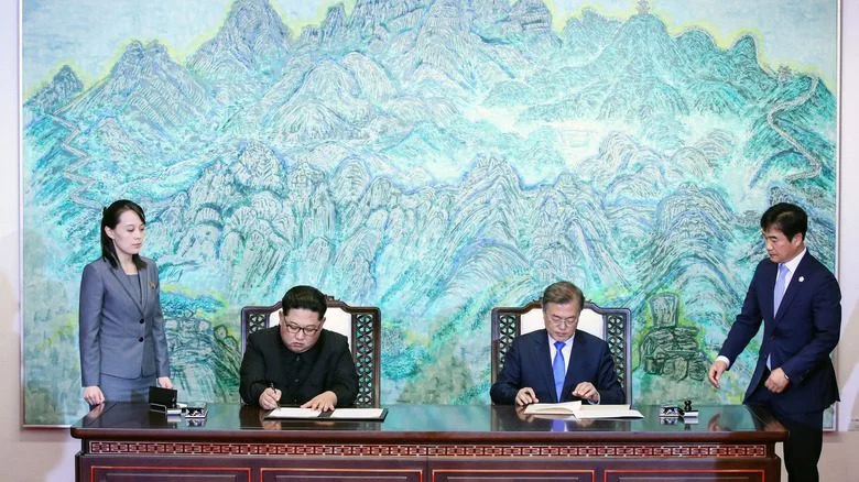 Kim Yo-jong se tient à côté d'une table pendant que Kim Jong-un et Moon Jae-in signent des documents
