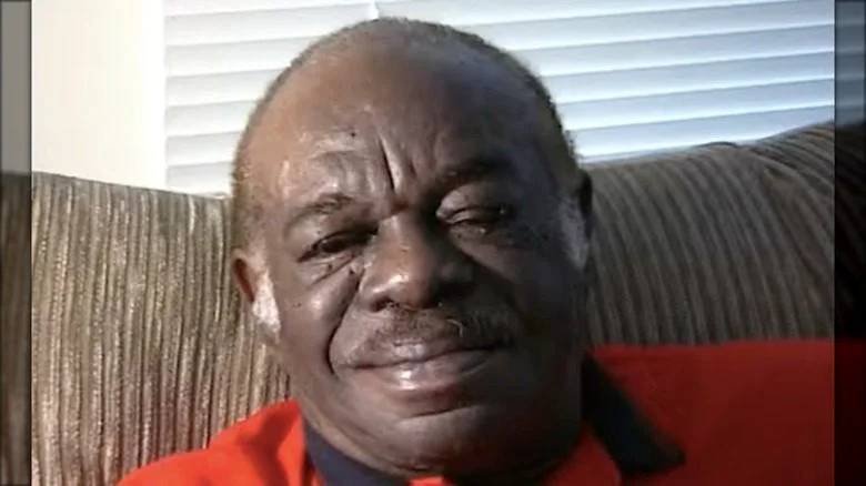 J.D. Hudson assis dans un pull rouge