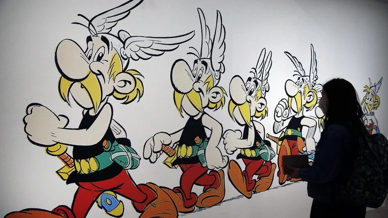 Un visiteur portant un masque de protection regarde un dessin représentant le personnage d'Asterix, par le designer français Uderzo