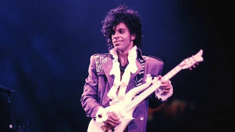 Prince en costume violet jouant de la guitare sur scène