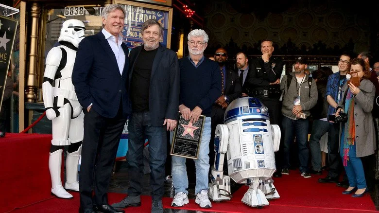 George Lucas posing with Mark Hamill and Harrison Ford