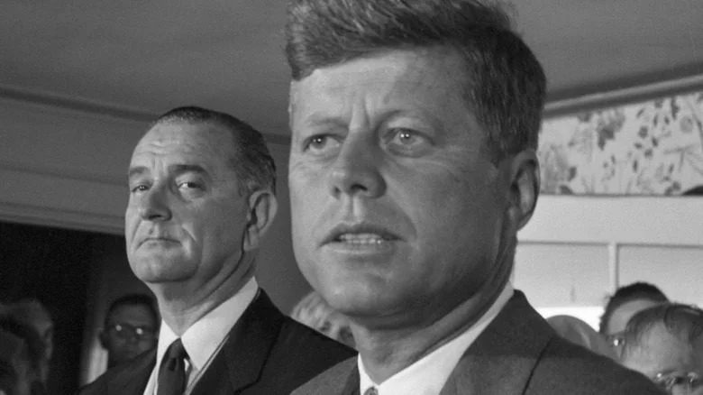 LBJ frowns behind JFK