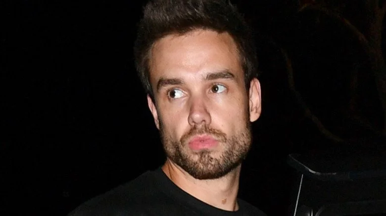 Liam Payne devant une voiture, sur fond noir