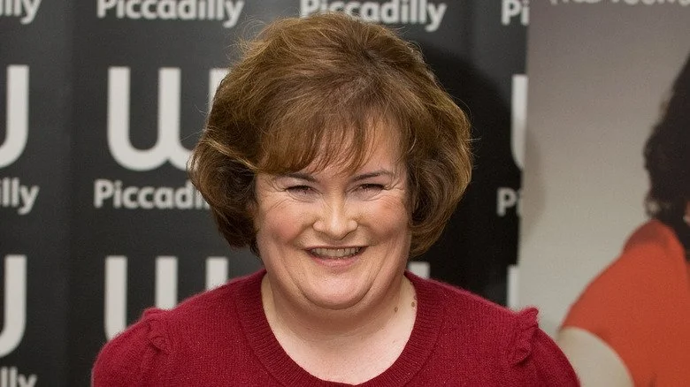 Susan Boyle souriante en pull rouge