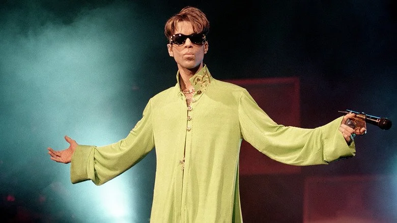 Prince sur scène avec des lunettes de soleil et une chemise verte