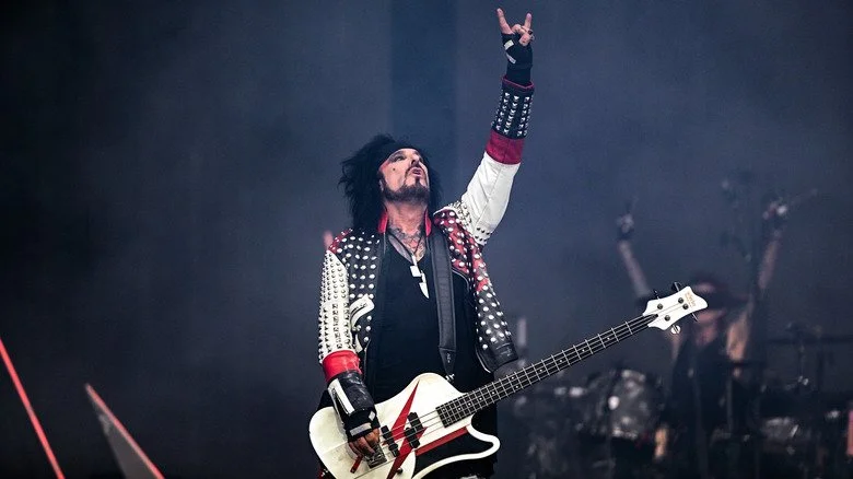 Nikki Sixx jouant de la guitare basse blanche, main levée avec des cornes du diable
