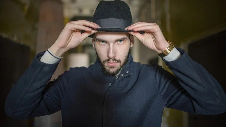 Homme avec une barbe en goatee, veste sombre et chapeau