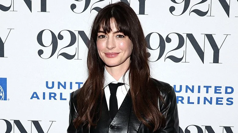 Anne Hathaway souriante, portant une veste et une cravate