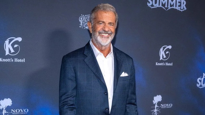 Mel Gibson souriant portant une chemise blanche et un blazer marine