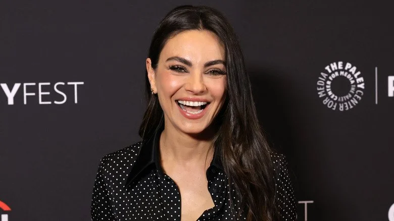 Mila Kunis souriante portant une chemise noire avec des pois blancs