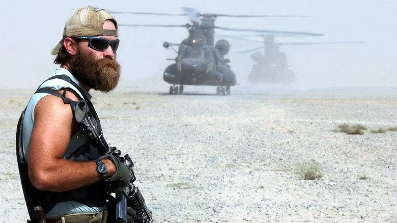 Un Green Beret tenant une arme devant un hélicoptère