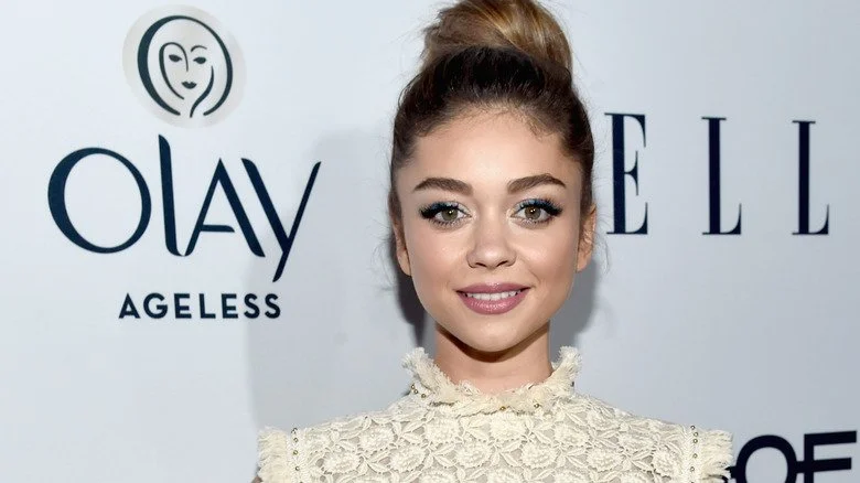 Sarah Hyland souriante dans une robe blanche lors de l'événement Olay