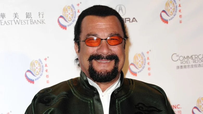 Steven Seagal en veste vert foncé, souriant