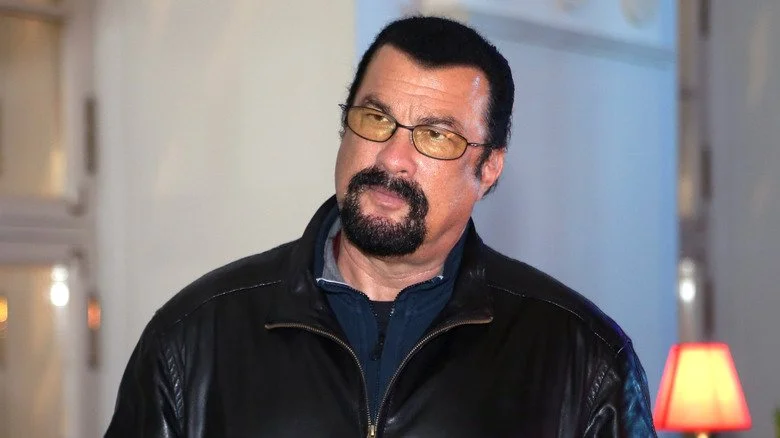 Steven Seagal en veste en cuir noir, visiblement agacé