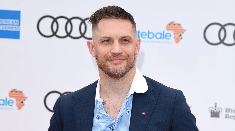 Tom Hardy souriant, portant une chemise bleue et un blazer