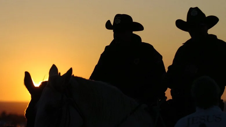 Deux adjoints de shérif à cheval regardent le soleil se coucher