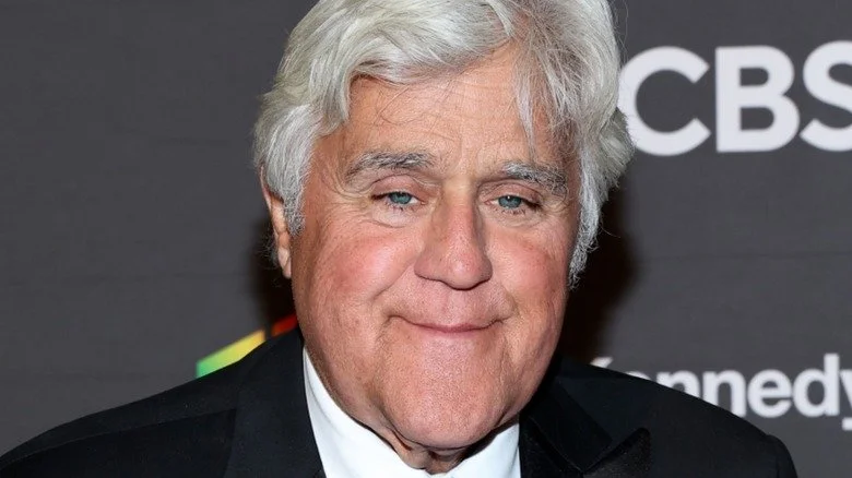 Jay Leno portant un costume noir et souriant tristement