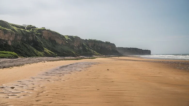 Vue moderne de la plage d'Omaha en Normandie, France, avec l'océan à droite et les falaises à gauche.