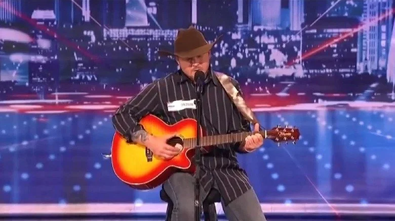 Timothy Poe portant un chapeau, jouant de la guitare et chantant sur America's Got Talent