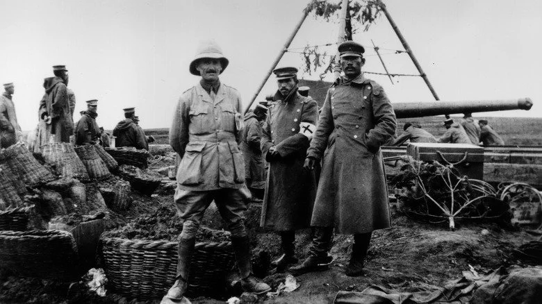 Un officier britannique avec deux de ses homologues japonais à côté d'un gros canon camouflé en 1914 à Tsingtau, en Chine