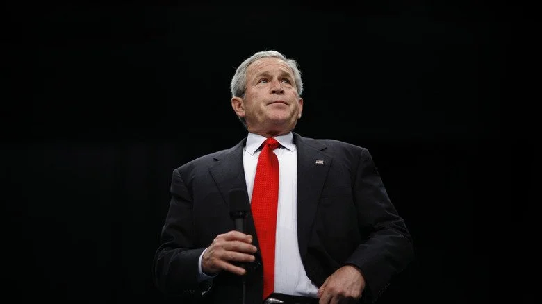 George W. Bush sur scène en costume avec un microphone