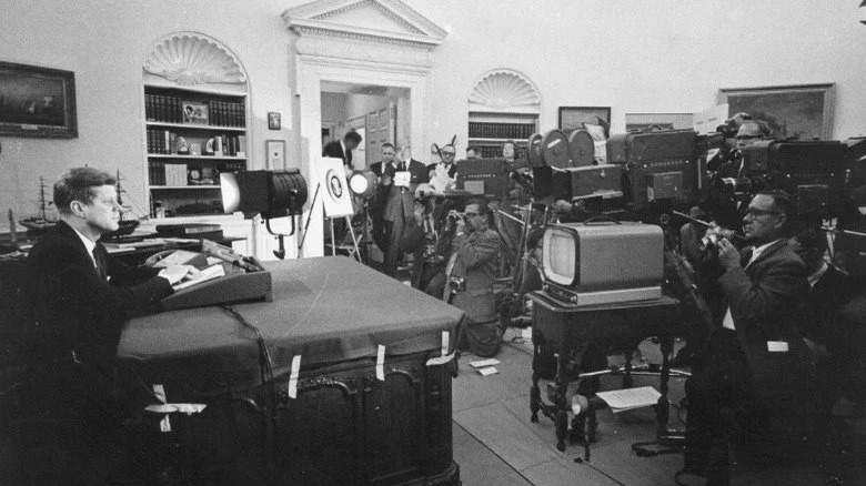 John F. Kennedy derrière son bureau avec la presse à l'écoute