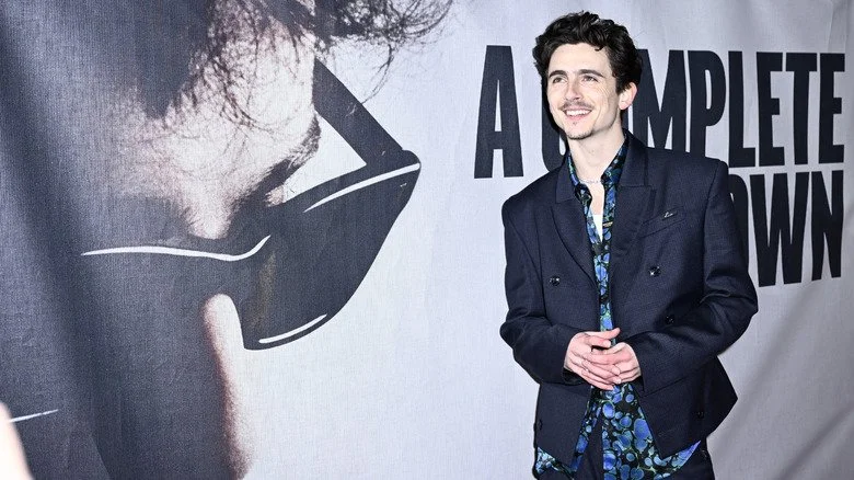 Timothée Chalamet posant devant l'affiche du film A Complete Unknown