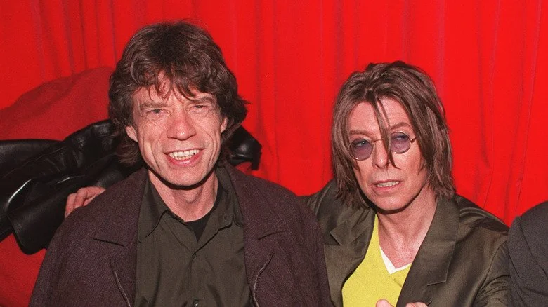 Mick Jagger et David Bowie souriant et pointant vers la caméra