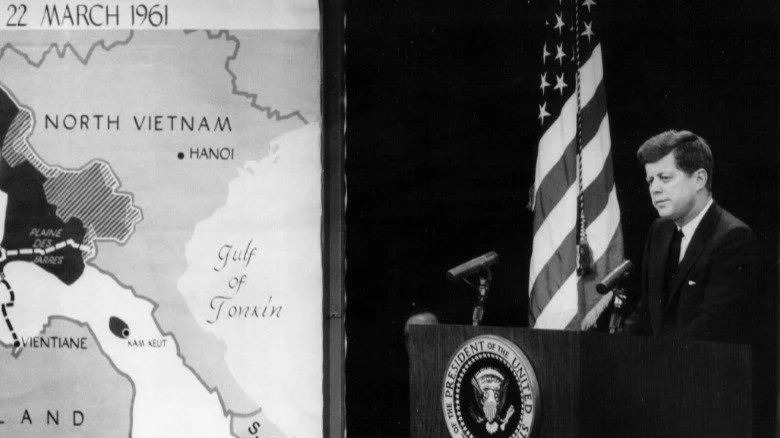 John F. Kennedy à un podium à côté d'une carte du Vietnam