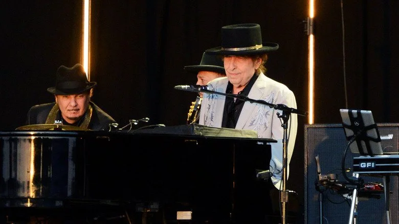 Bob Dylan sur scène au piano, vêtu d’un costume et d’un chapeau