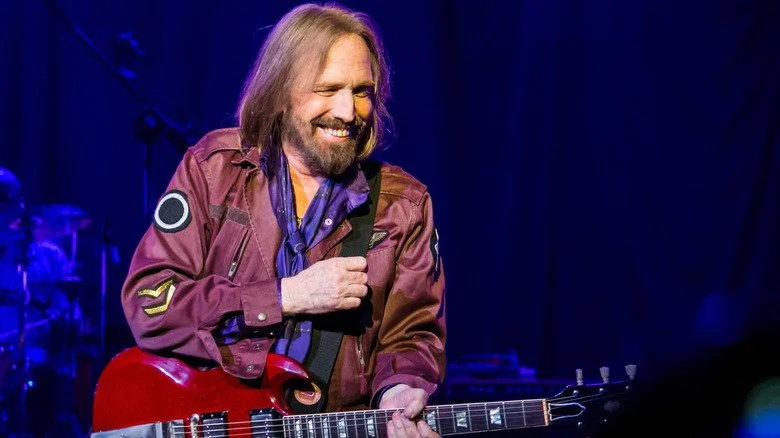 Tom Petty souriant et tenant une guitare rouge tout en se produisant sur scène