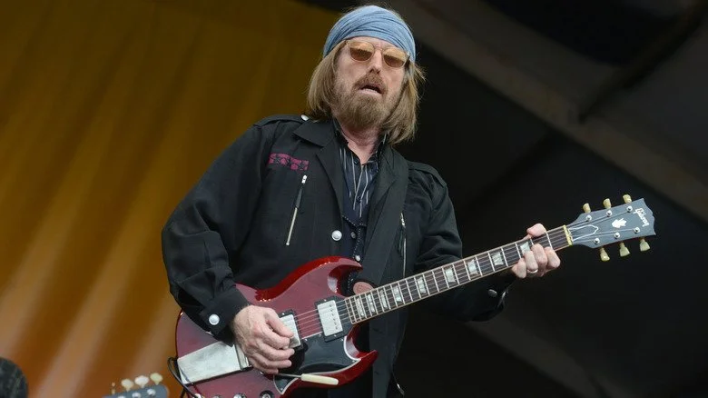 Tom Petty joue d'une guitare rouge sur scène tout en portant des lunettes de soleil et un bandana bleu
