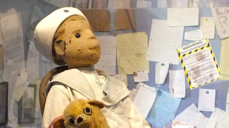 Robert la Poupée dans une vitrine de musée sur une petite chaise.