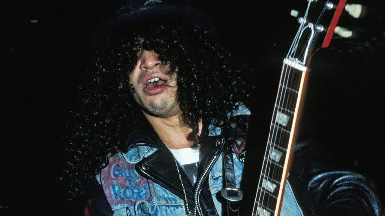 Slash jouant de la guitare avec la bouche ouverte dans les années 1980