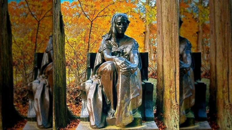 Statue de la Dame de Bronze au cimetière de Sleepy Hollow, avec des feuilles d'automne orange et jaunes en arrière-plan.
