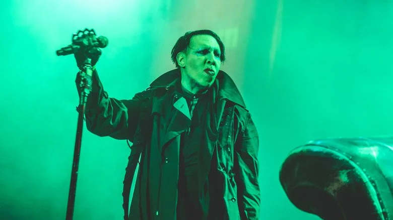 Marilyn Manson in large coat onstage with microphone
