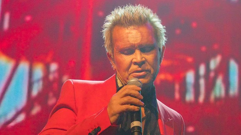 Billy Idol chante devant un fond rouge