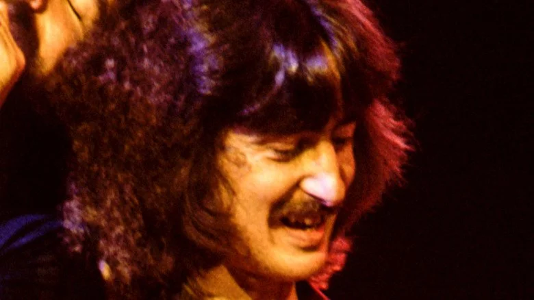 Barry Goudreau sourit et regarde sa guitare sur scène