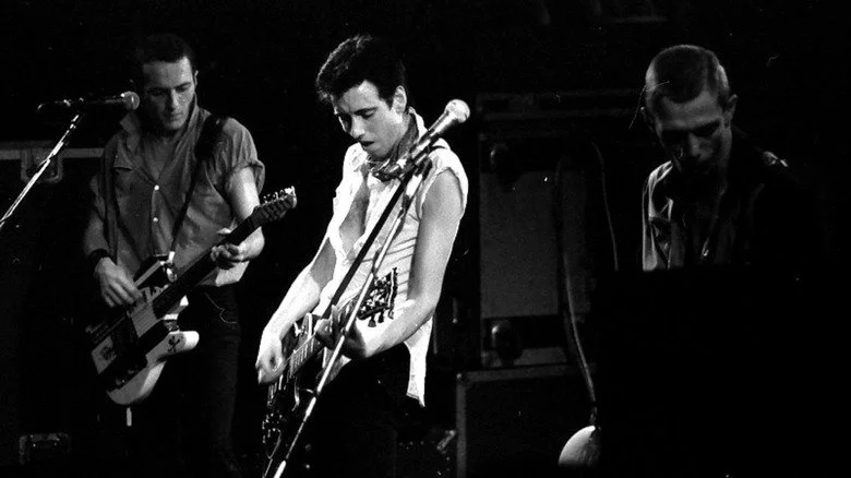 Photo de Joe Strummer, Mick Jones, et Paul Simonon de The Clash sur scène en 1980, CC BY-SA 4.0